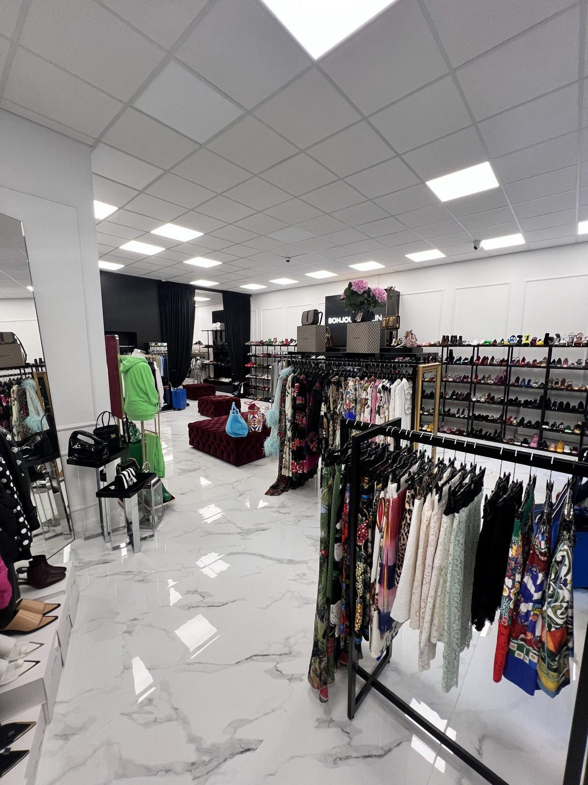 Innenansicht des Bonjour Berlin High Fashion Geschäfts. Stilvolle Displays präsentieren exklusive Mode von Dolce & Gabbana, ergänzt durch eine elegante Einrichtung und warme Beleuchtung, die eine gehobene Atmosphäre schaffen. Kunden durchstöbern die Designerstücke in einem edlen Ambiente.