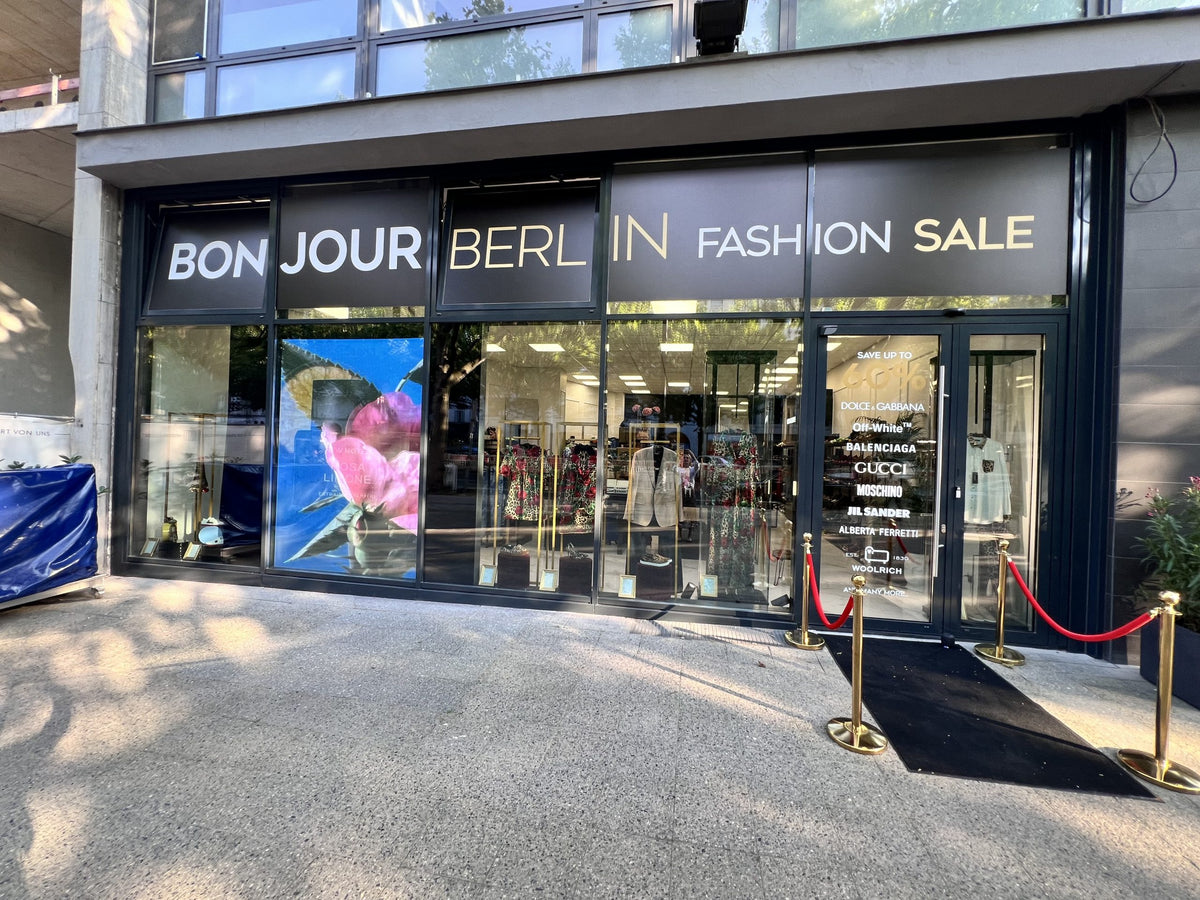 Außenansicht des Bonjour Berlin High Fashion Geschäfts. Die stilvolle Fassade und das ansprechende Schaufenster präsentieren exklusive Mode von Dolce & Gabbana. Das moderne Design des Eingangsbereichs zieht die Aufmerksamkeit der Passanten auf sich und lädt zum Erkunden ein.