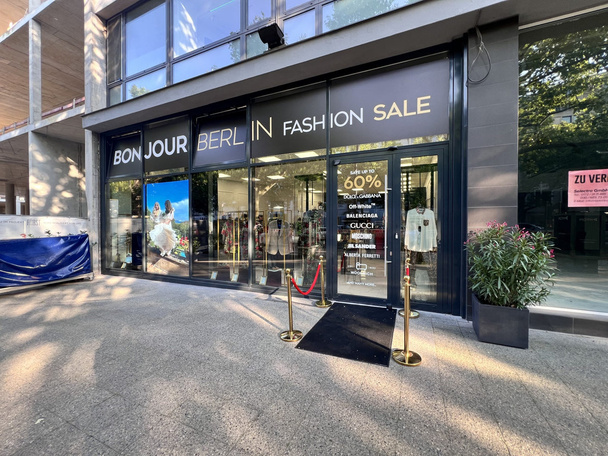 Außenansicht des Bonjour Berlin High Fashion Geschäfts. Das Schaufenster ist stilvoll mit Designerstücken von Dolce & Gabbana dekoriert. Die elegante Fassade lockt Kunden an und unterstreicht den exklusiven Charakter des Geschäfts.